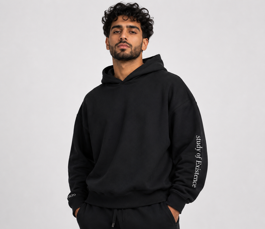 Man wearing a black hoodie with 'study of Existence' text on a gray background. Stylist streetwear hoodie, comfy formal hoodie, fashion hoodie, graphic hoodie, no front pocket hoodie, large hooded hoodie, large hood hoodie, oversized hoodie