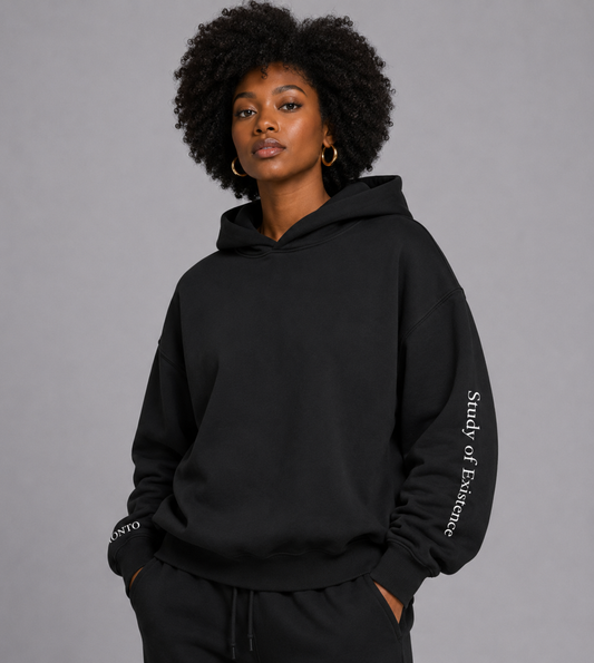 Person wearing a black hoodie with text on sleeves against a gray background. Stylist streetwear hoodie, comfy formal hoodie, fashion hoodie, graphic hoodie, no front pocket hoodie, large hooded hoodie, large hood hoodie, oversized hoodie