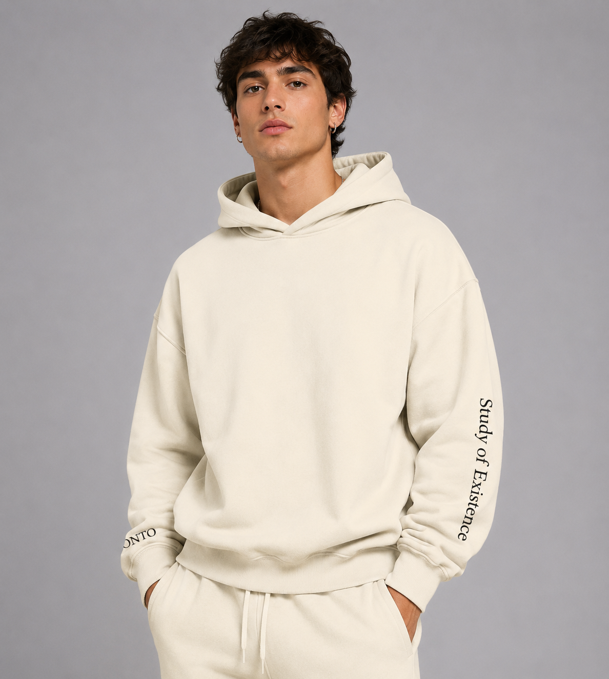 Man wearing a beige hoodie with text on sleeves against a gray background. Stylist streetwear hoodie, comfy formal hoodie, fashion hoodie, graphic hoodie, no front pocket hoodie, large hooded hoodie, large hood hoodie, oversized hoodie